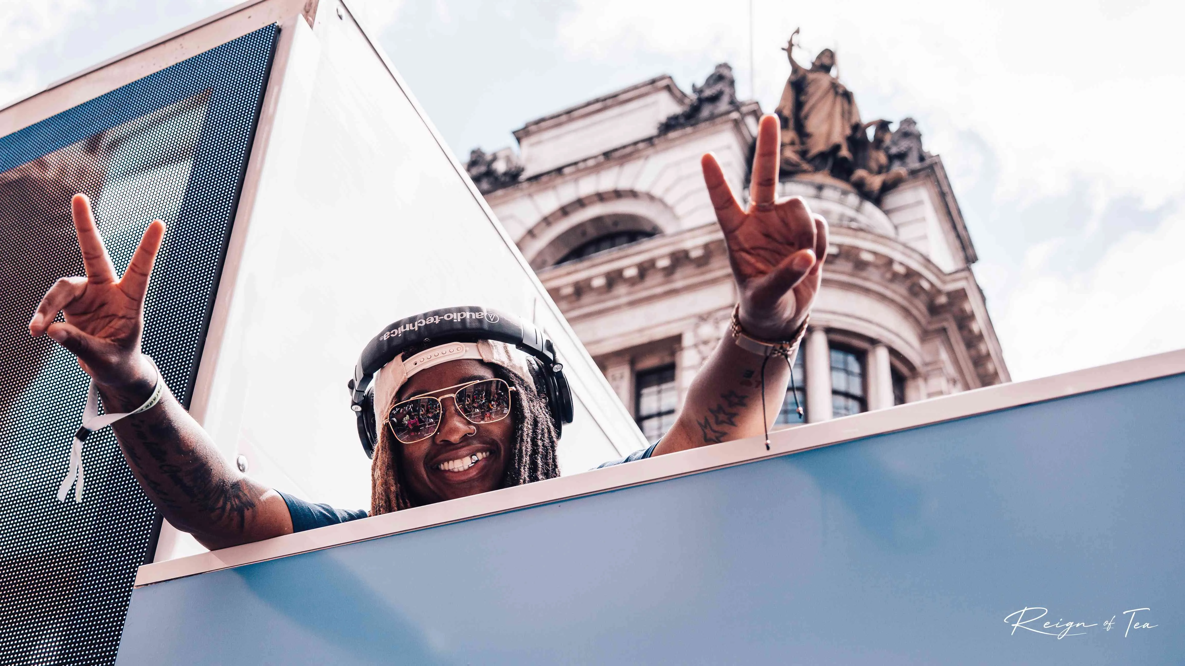 Low-angle shot of a smiling DJ with headphones and peace signs at an outdoor festival