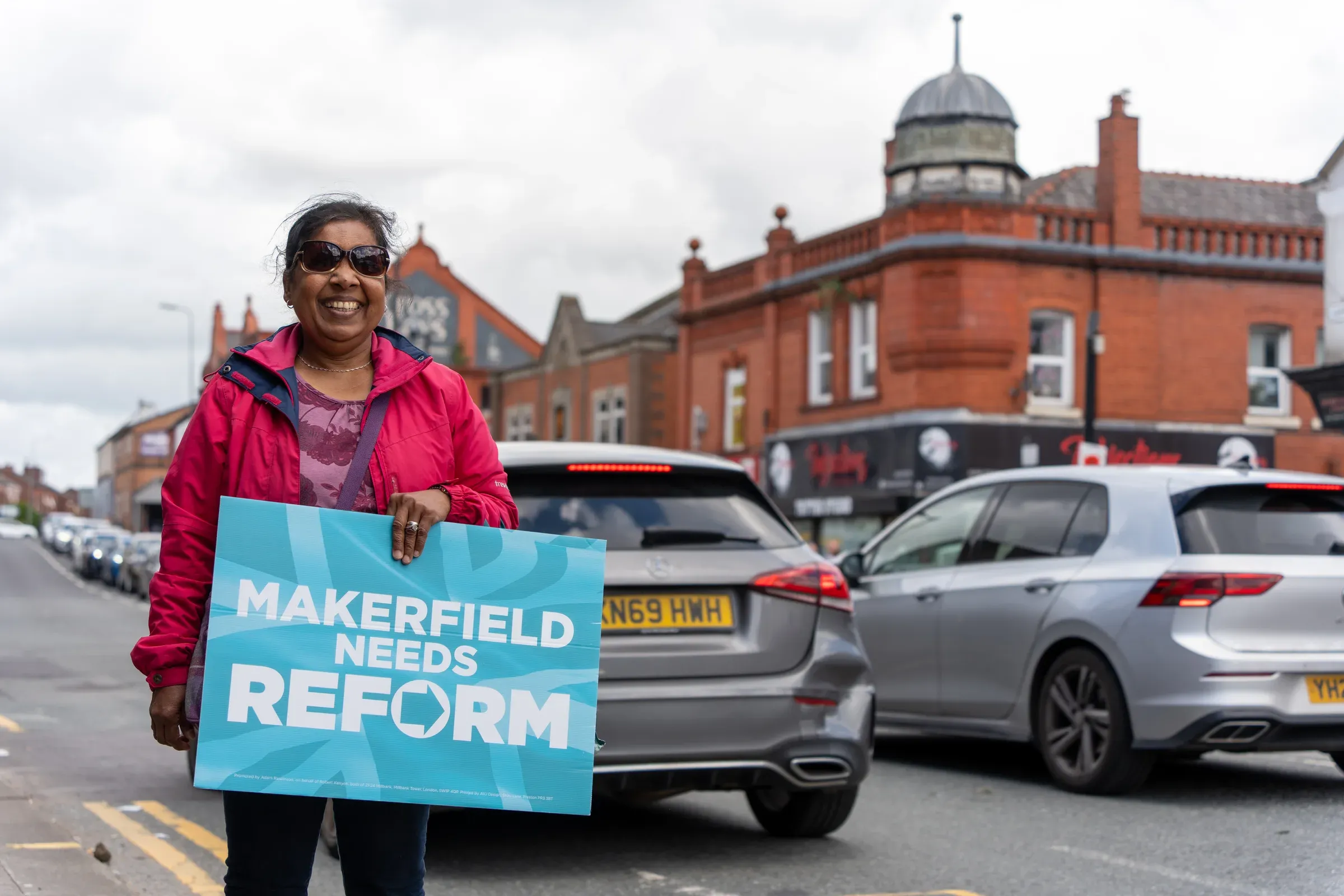 Rally banners and cars lined along a street at Makerfield Day of Action