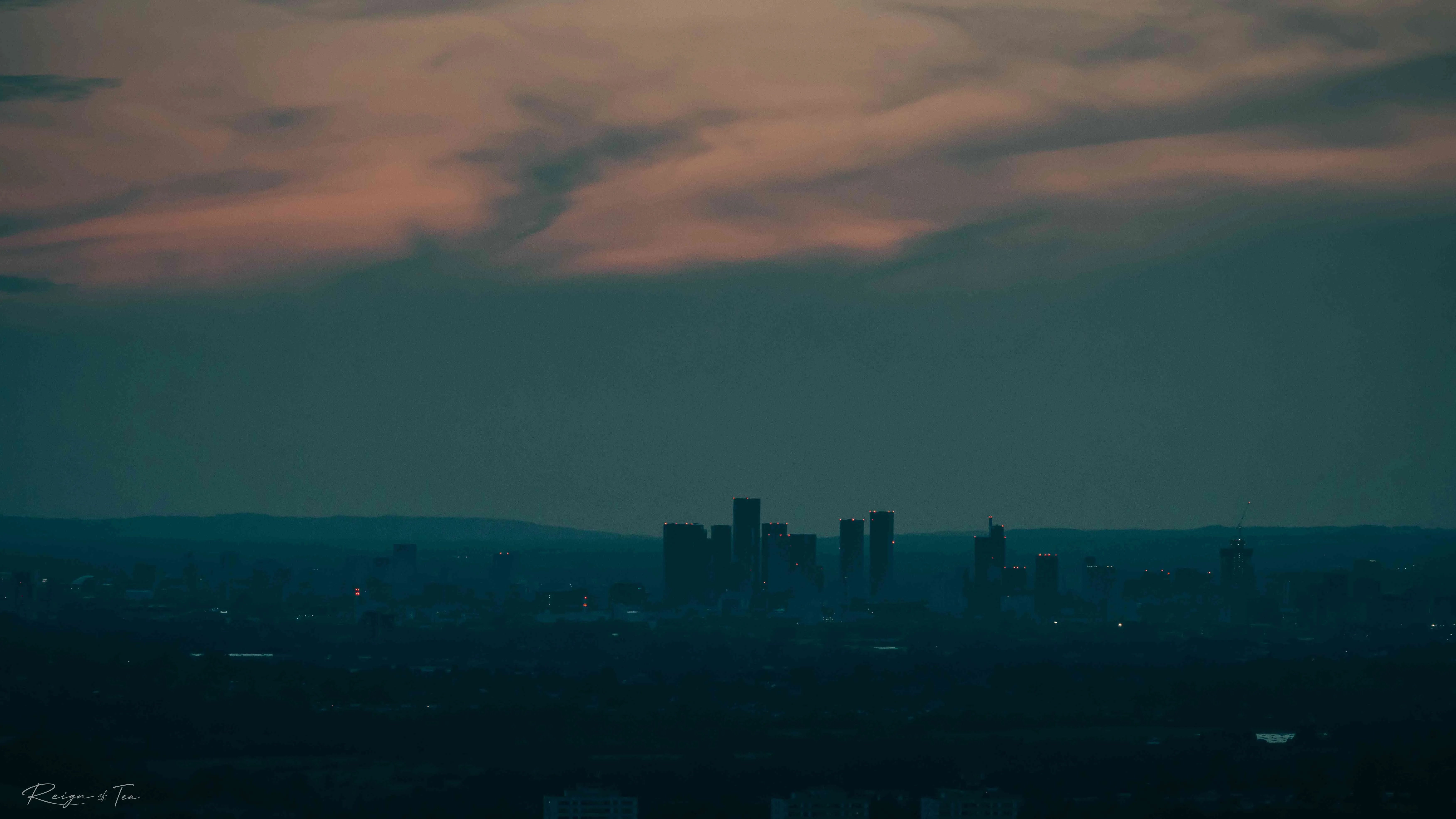 Manchester skyline at twilight — silhouetted towers under a teal sky streaked with orange cloud